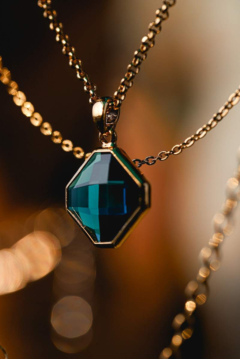 Colgante de piedra verde azulada con cadenas doradas y fondo desenfocado
