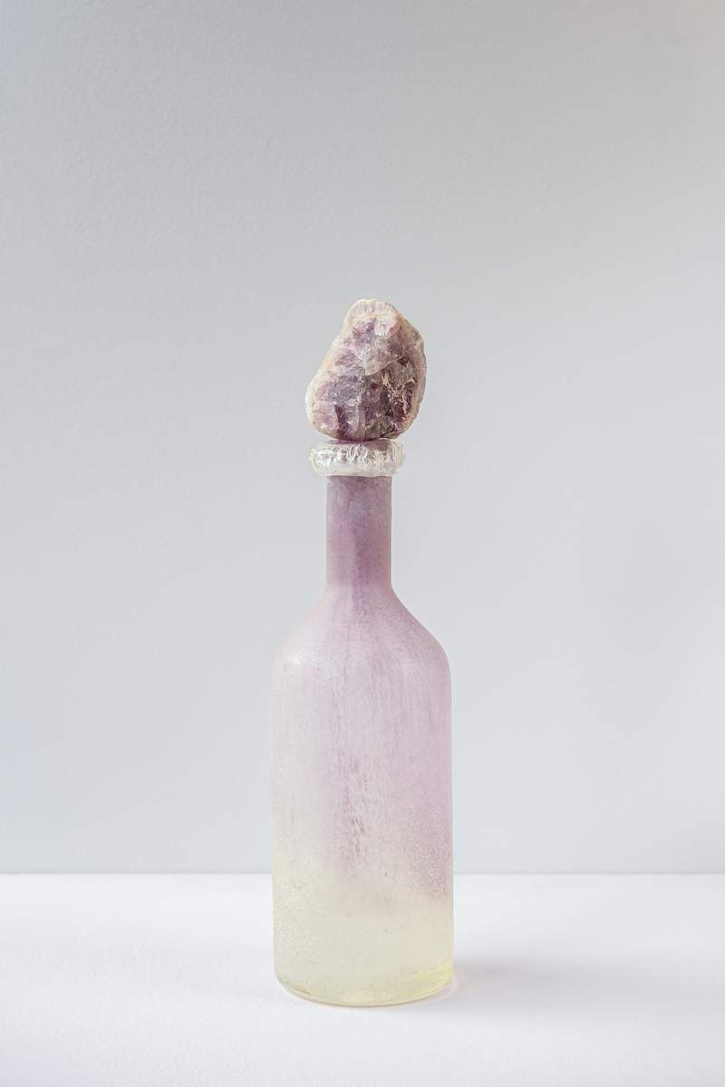 Botella de vidrio esmerilado en tonos lila y amarillo sobre fondo gris claro