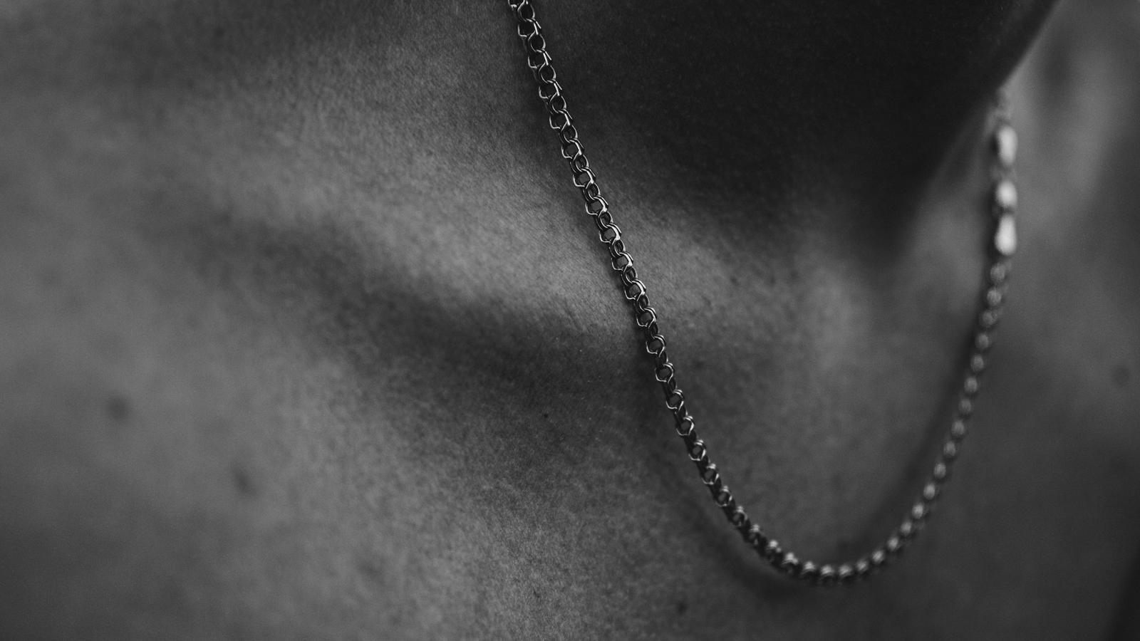Una cadena de plata de eslabones finos sobre una clavícula, en blanco y negro.