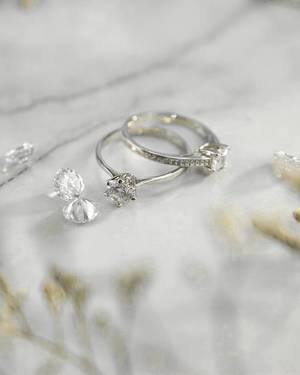 Dos anillos y piedras sueltas sobre mármol claro.