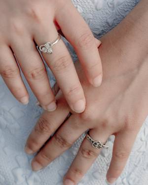 Dos manos con anillos finos sobre encaje blanco.