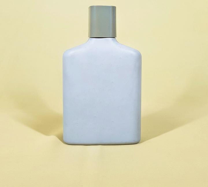 Frasco plano de color celeste pálido con tapa gris, sobre un fondo amarillo suave