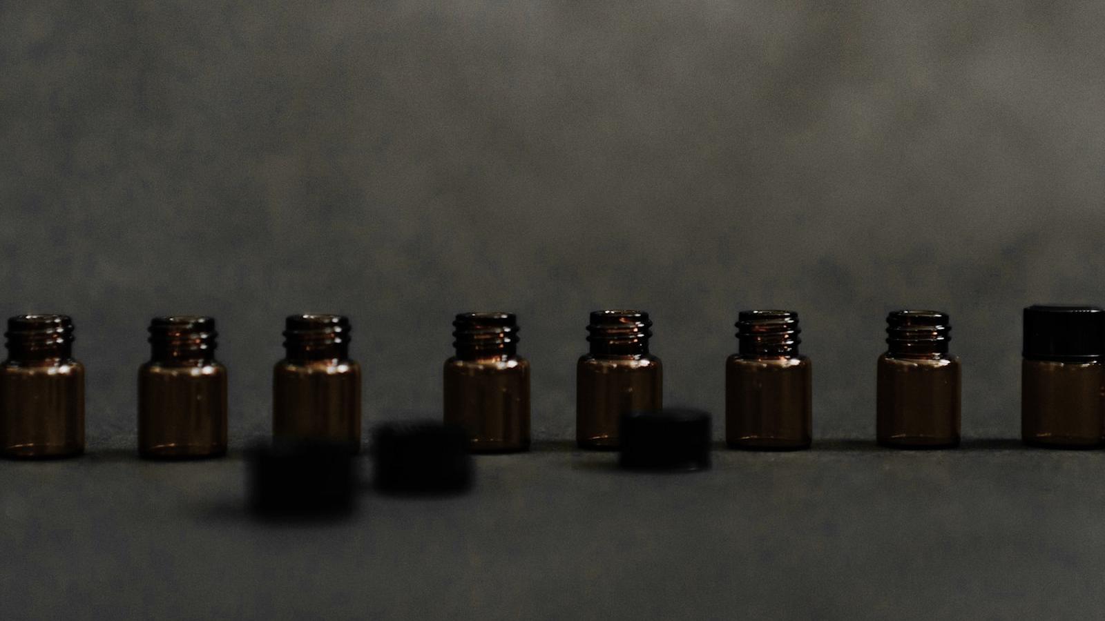 Fila de pequeños frascos de vidrio ámbar sobre una superficie gris oscura, con sus tapas sueltas