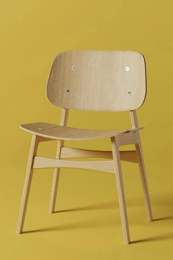 Una silla de roble claro de respaldo curvo sobre un fondo amarillo