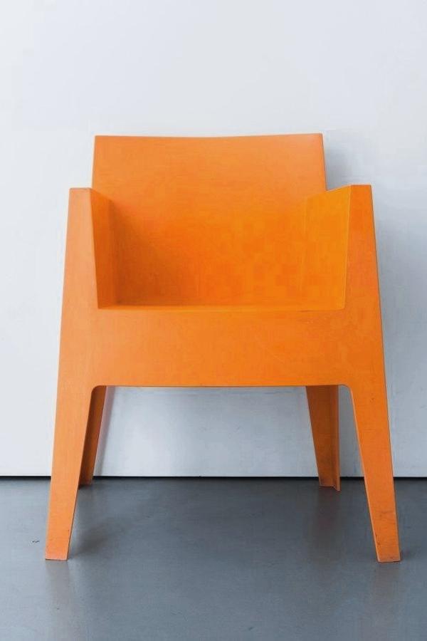 Un sillón de resina naranja contra una pared clara