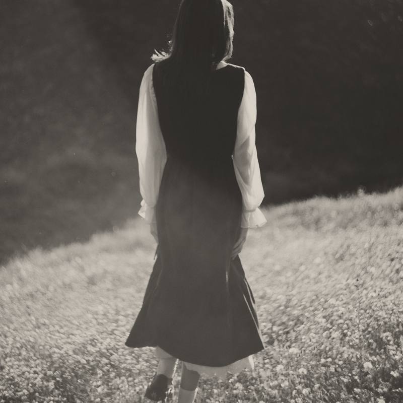 Una mujer de espaldas caminando con un vestido oscuro y mangas blancas, en blanco y negro cálido