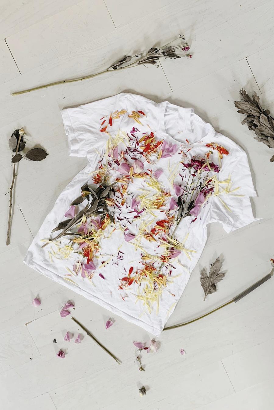 Una camiseta blanca extendida sobre una mesa, cubierta de pétalos y flores secas