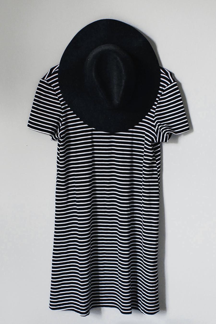 Un vestido de rayas negras y blancas colgado en la pared con un sombrero negro de ala ancha encima