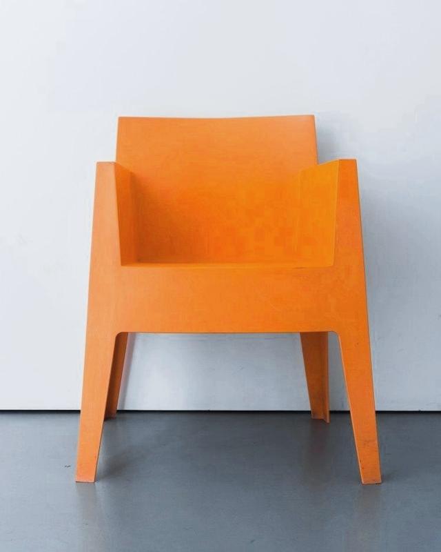 Un sillón de resina naranja contra una pared clara