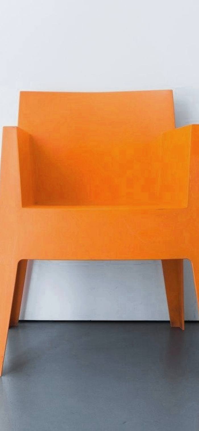 Un sillón de resina naranja contra una pared clara