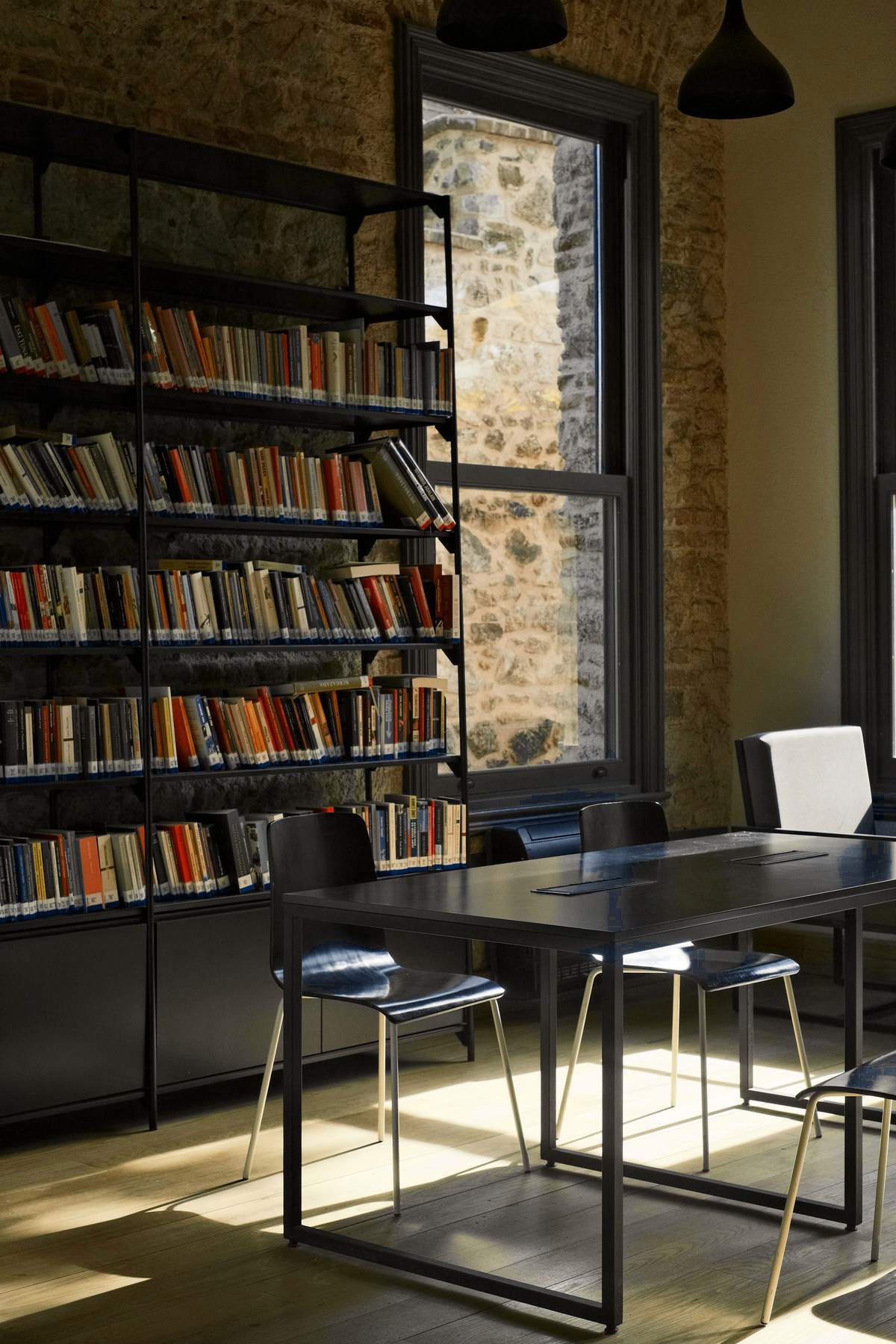 Estantería de acero negro llena de libros junto a una ventana y una mesa de lectura