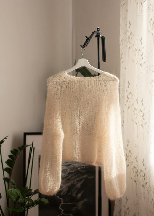Cárdigan crema de mohair colgado junto a una ventana con cortina