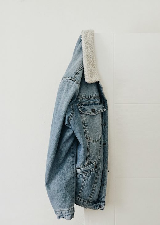 Chaqueta de mezclilla clara con cuello de borrego colgada de una pared blanca