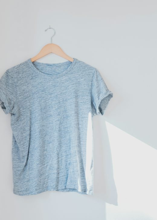 Polera celeste jaspeada colgada de una percha de madera contra una pared blanca