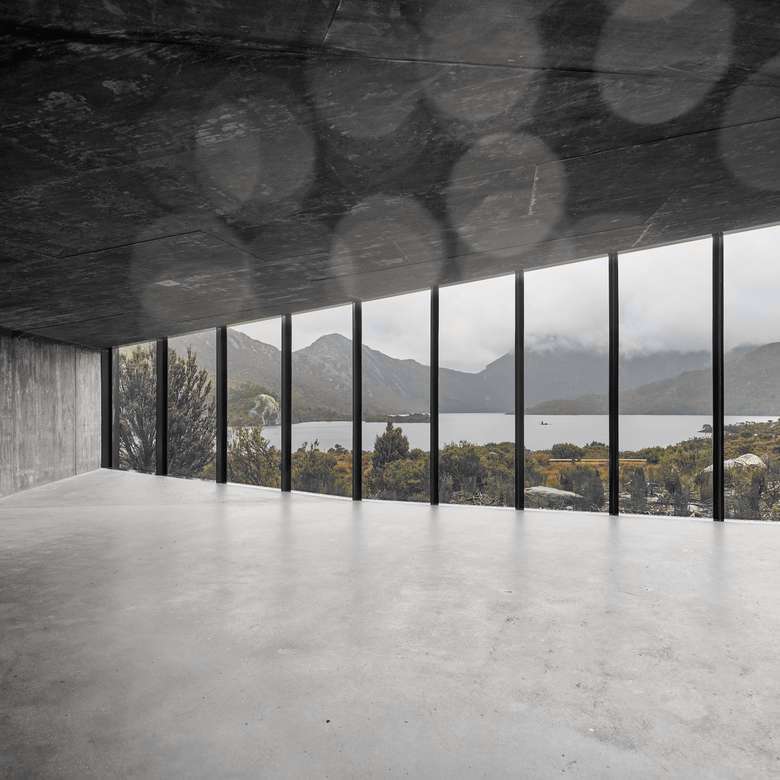 Sala de hormigón con una gran ventana hacia las montañas