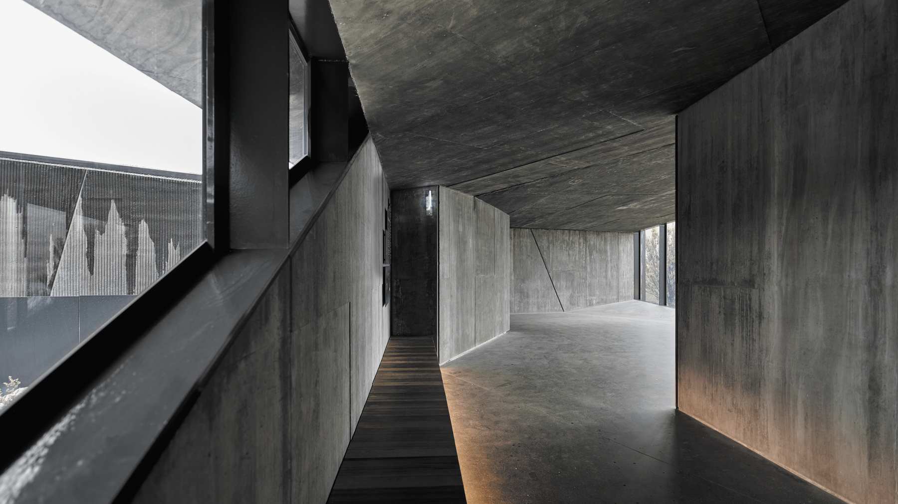 Pasillo de hormigón con piso de madera y una ventana lateral