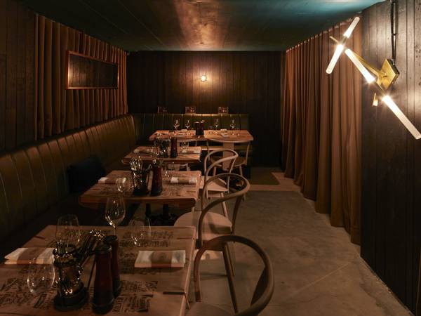 Salón alargado de un restaurante con reservados de madera y una lámpara en el muro