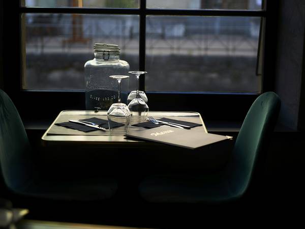 Mesa para dos junto a una ventana, con vasos y cubiertos, en un salón en penumbra