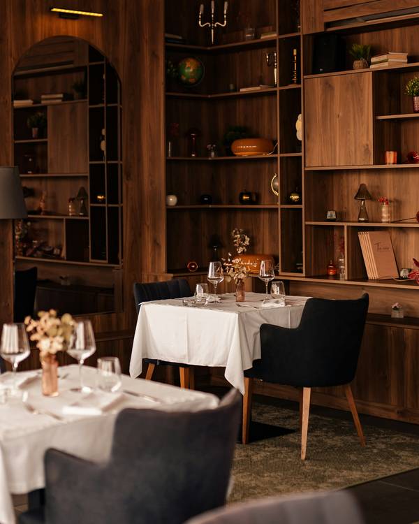 Comedor con mesas de mantel blanco, sillas oscuras y una estantería de madera al fondo