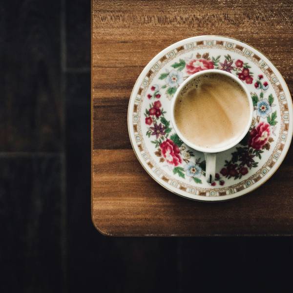 Taza sobre un plato de porcelana floreado, sobre una mesa de madera oscura