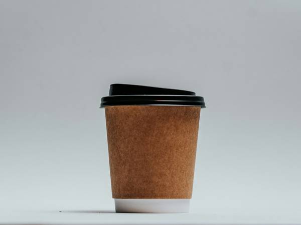 Vaso de café para llevar, de cartón kraft, sobre un fondo gris claro