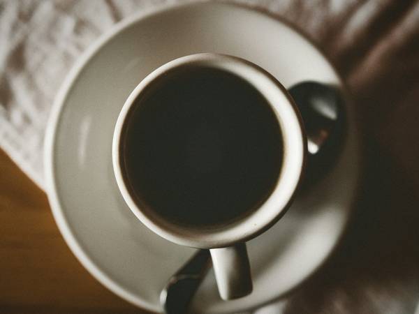 Taza de café negro sobre un plato blanco apoyado en un paño, vista cercana