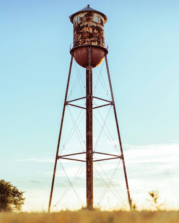Torre de agua oxidada sobre un campo de pasto seco