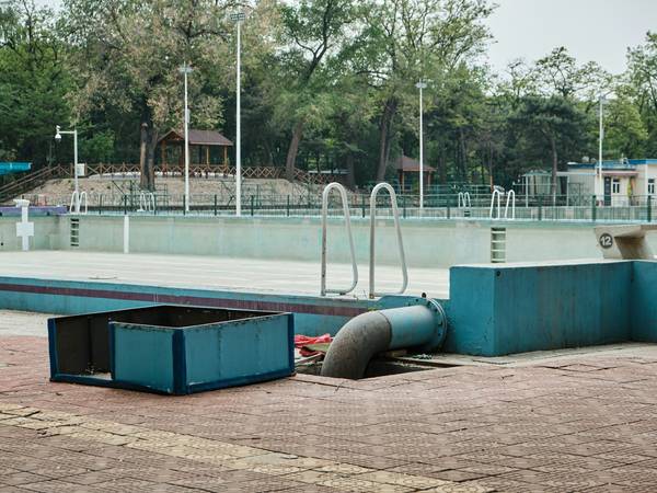 Piscina sin agua y una caja azul de bombas junto a árboles