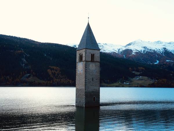 Torre de iglesia saliendo del agua frente a montañas con nieve
