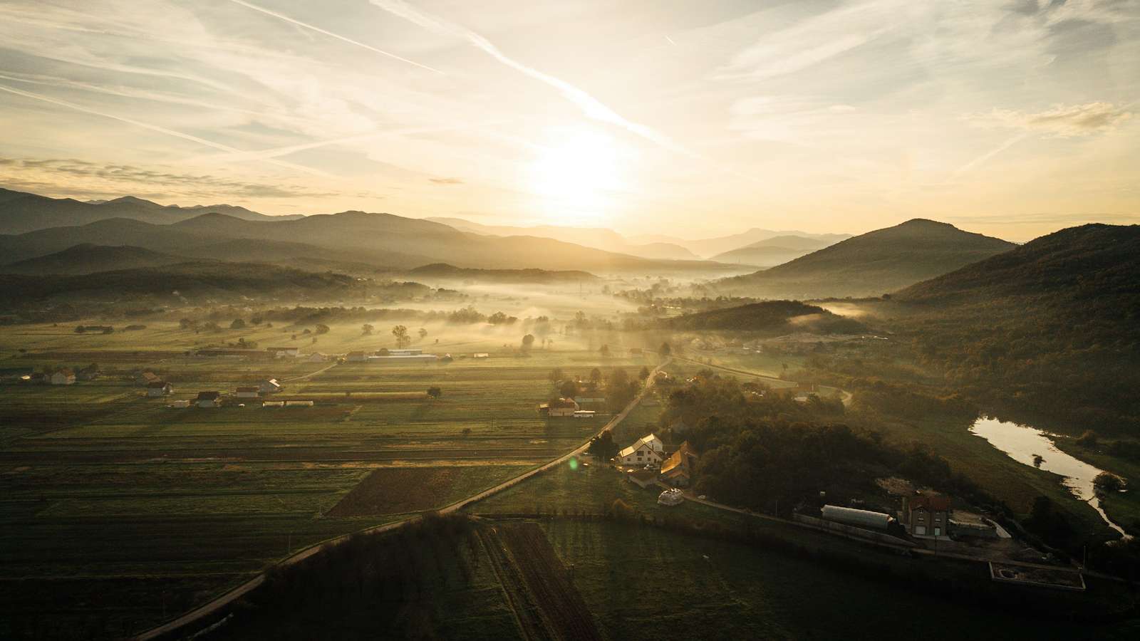 Sol sobre un valle de campos y colinas con neblina