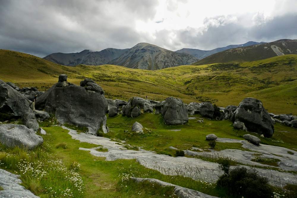 Bloques de piedra gris sobre una ladera verde con montañas al fondo