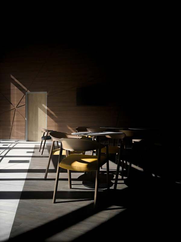 Mesa y sillas en una sala en penumbra, con una franja de luz en el suelo