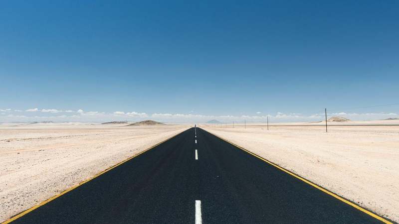 Camino recto de asfalto atravesando un desierto bajo un cielo azul