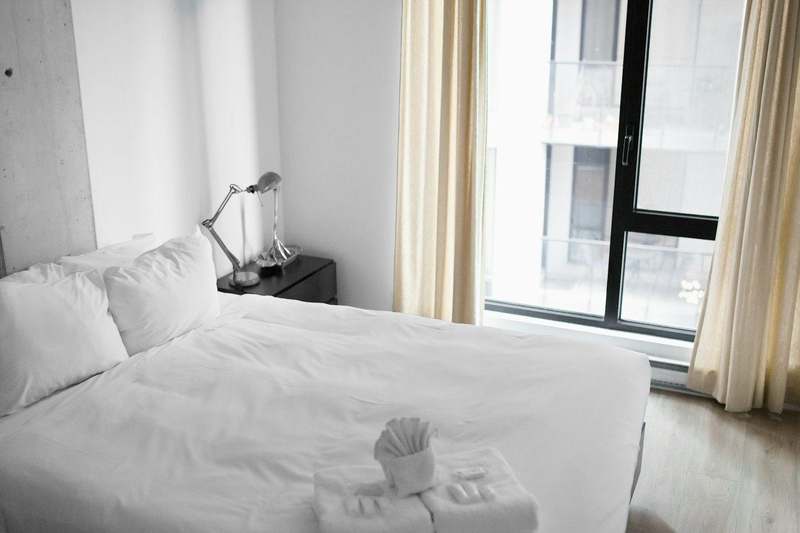 Cama blanca junto a una ventana con cortinas claras