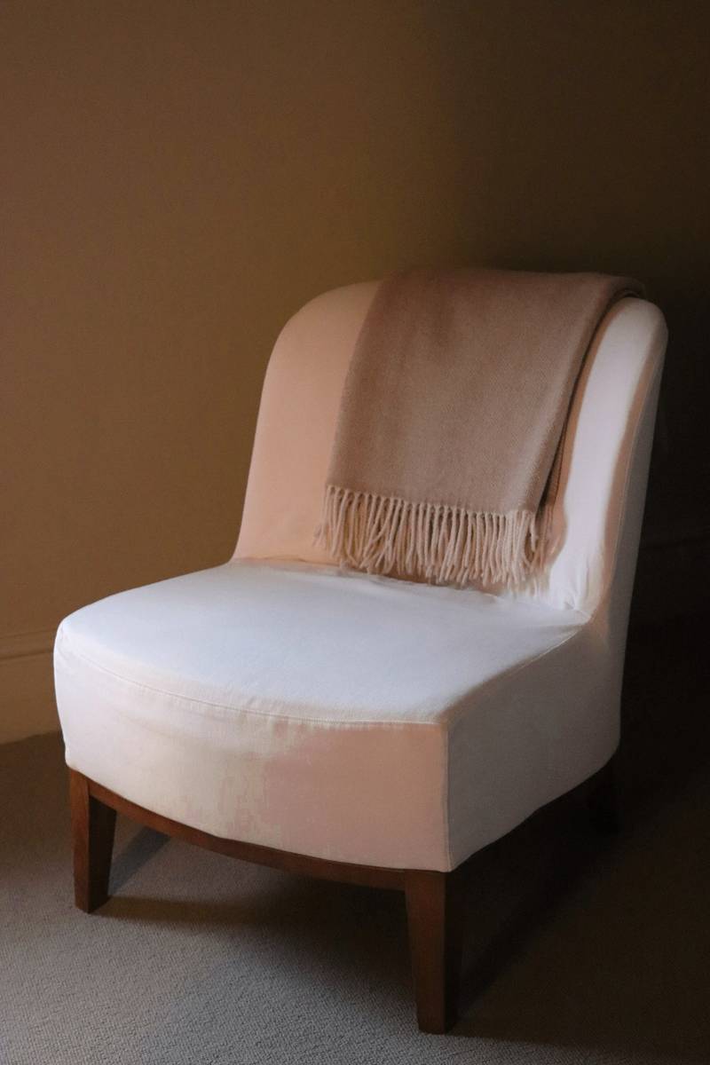 Sillón bajo blanco con un chal sobre el respaldo, en luz tibia