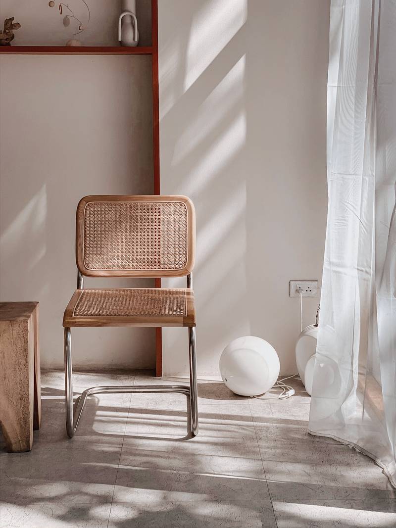 Silla de rejilla de mimbre junto a una cortina de lino que filtra la luz