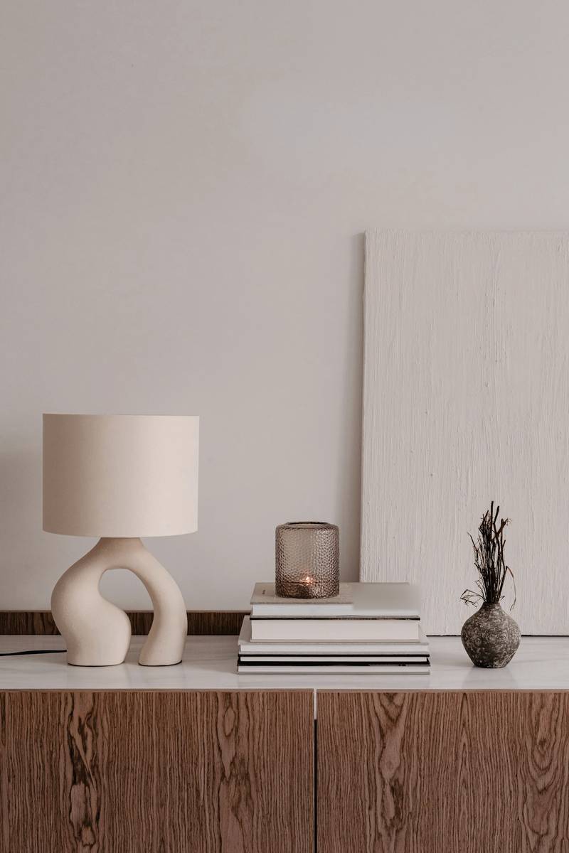 Lámpara de cerámica, libros y una vasija sobre un mueble de madera veteada