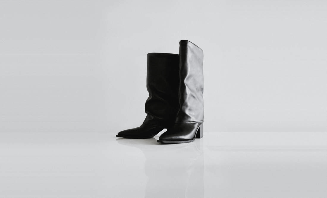 Botas negras altas de caña ancha sobre un fondo blanco brillante