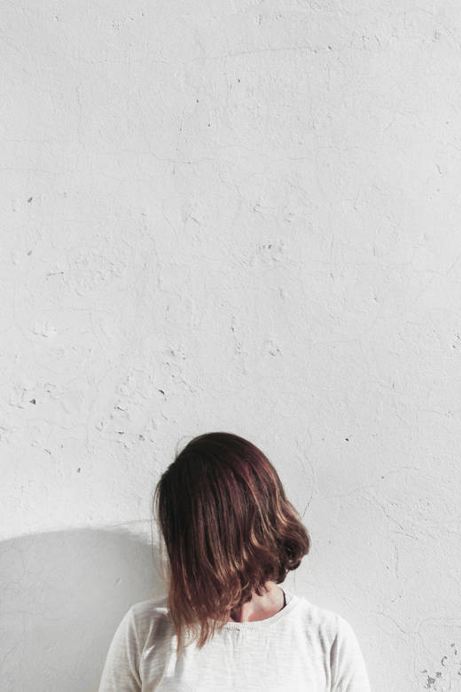 Mujer con el pelo cubriéndole la cara, con una camiseta clara, frente a un muro blanco