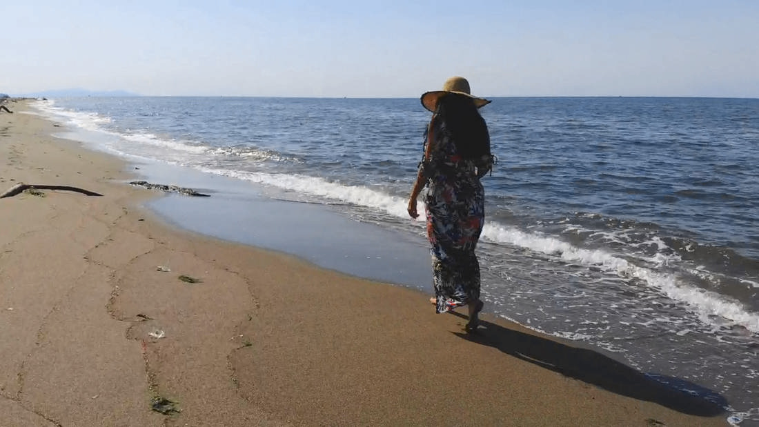 Mujer con sombrero de paja y vestido estampado, de espaldas, junto a las olas