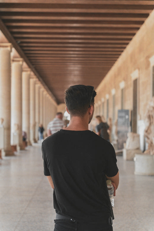 Hombre de espaldas con camiseta negra en un pórtico de columnas con techo de madera