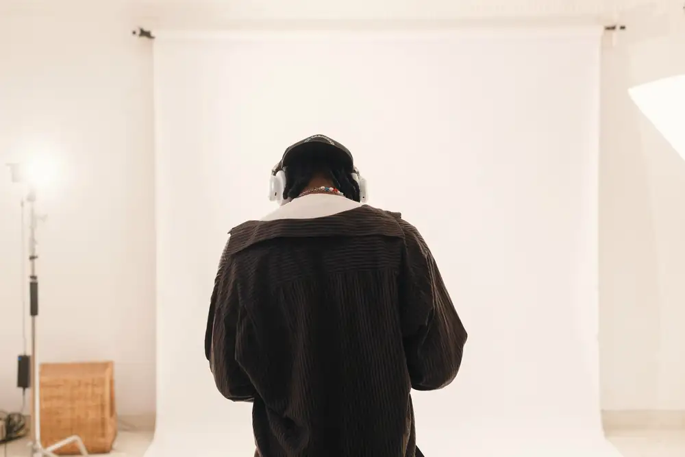 Persona de espaldas, con auriculares, en un estudio de fondo blanco