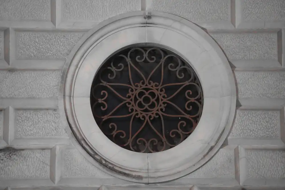 Ventana redonda con reja de hierro forjado en un muro de piedra