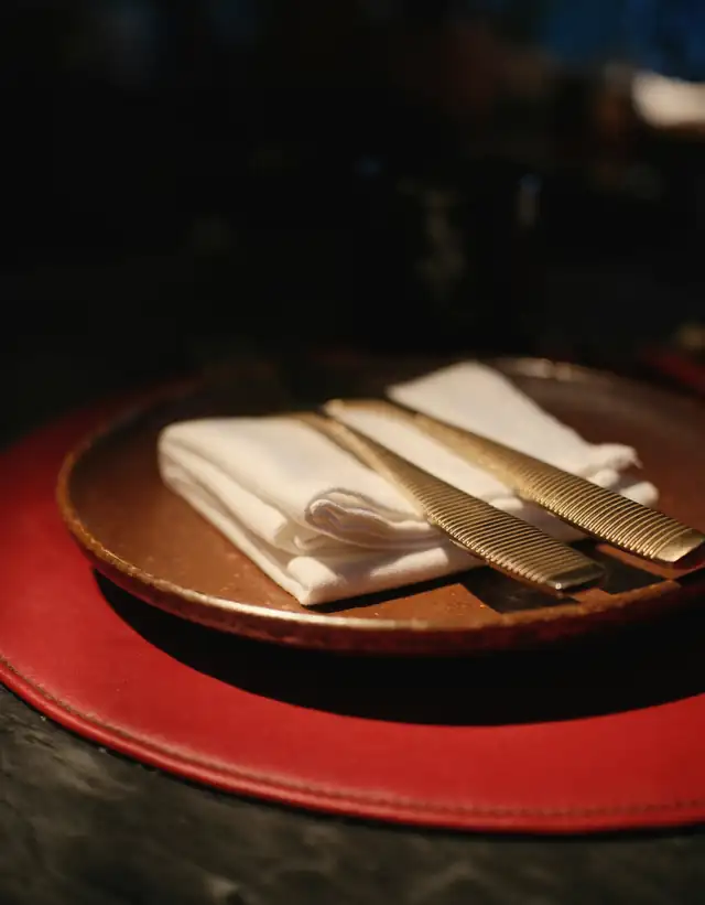 Plato rojo con servilleta blanca y cubiertos dorados sobre una mesa oscura
