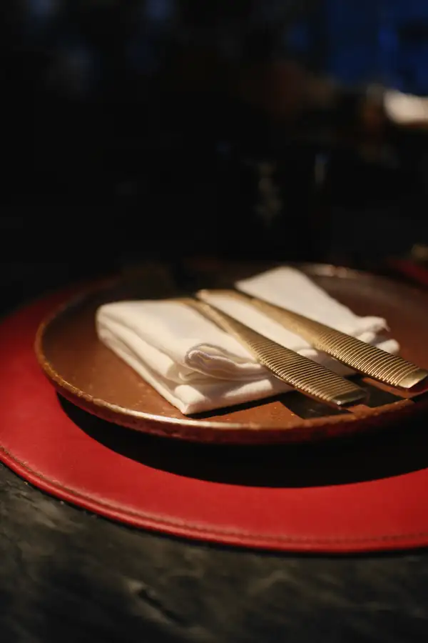 Plato rojo con servilleta blanca y cubiertos dorados sobre una mesa oscura