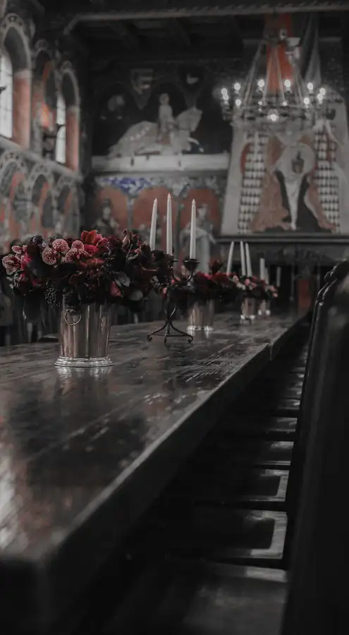 Mesa larga de madera oscura con flores, en una sala antigua