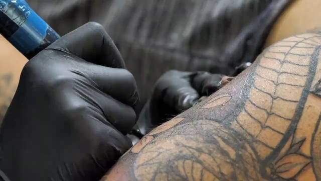 Manos con guantes negros sobre un antebrazo tatuado