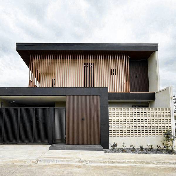 Una casa de dos plantas con listones de madera, un muro de bloques calados y una puerta de madera oscura