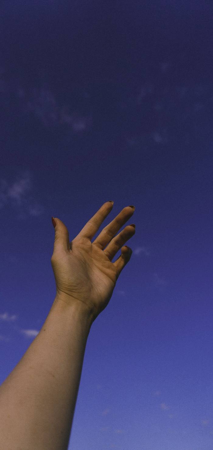 Una mano alzada hacia un cielo azul profundo
