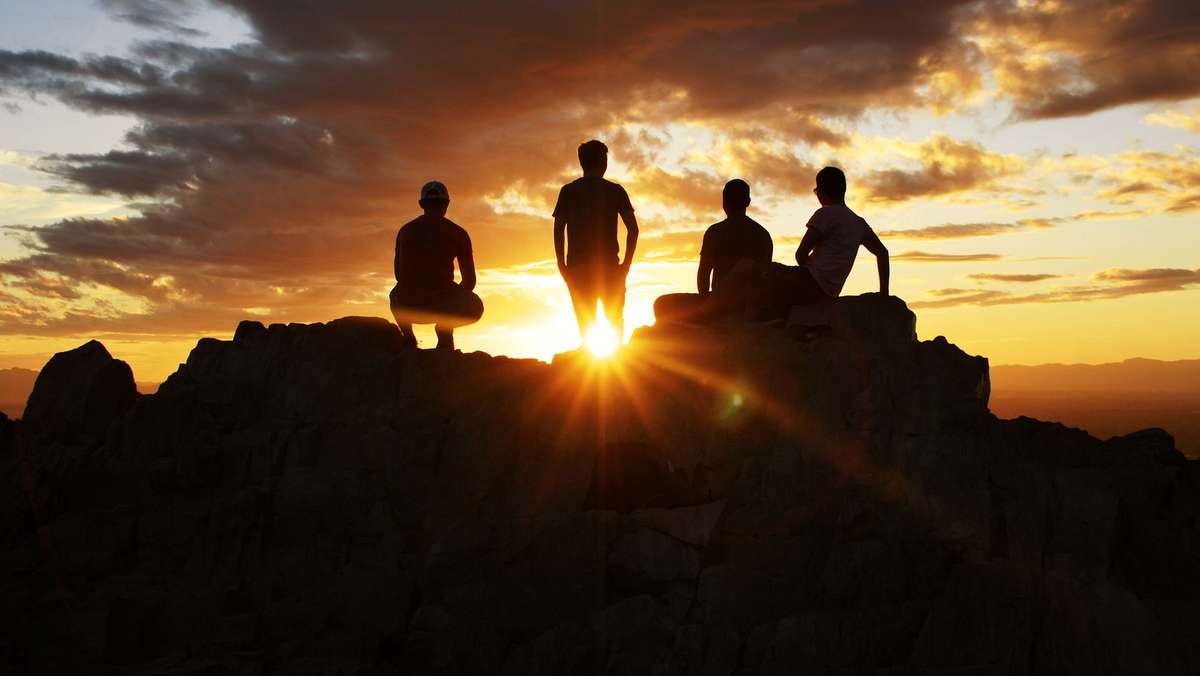 Figuras sentadas a contraluz en una cumbre al atardecer
